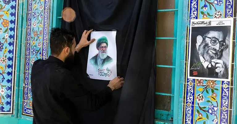 তেহরানে এক ব্যক্তি আয়াতুল্লাহ আলী খামেনি প্রতিকৃতিসহ একটি লিফলেট লাগাচ্ছেন